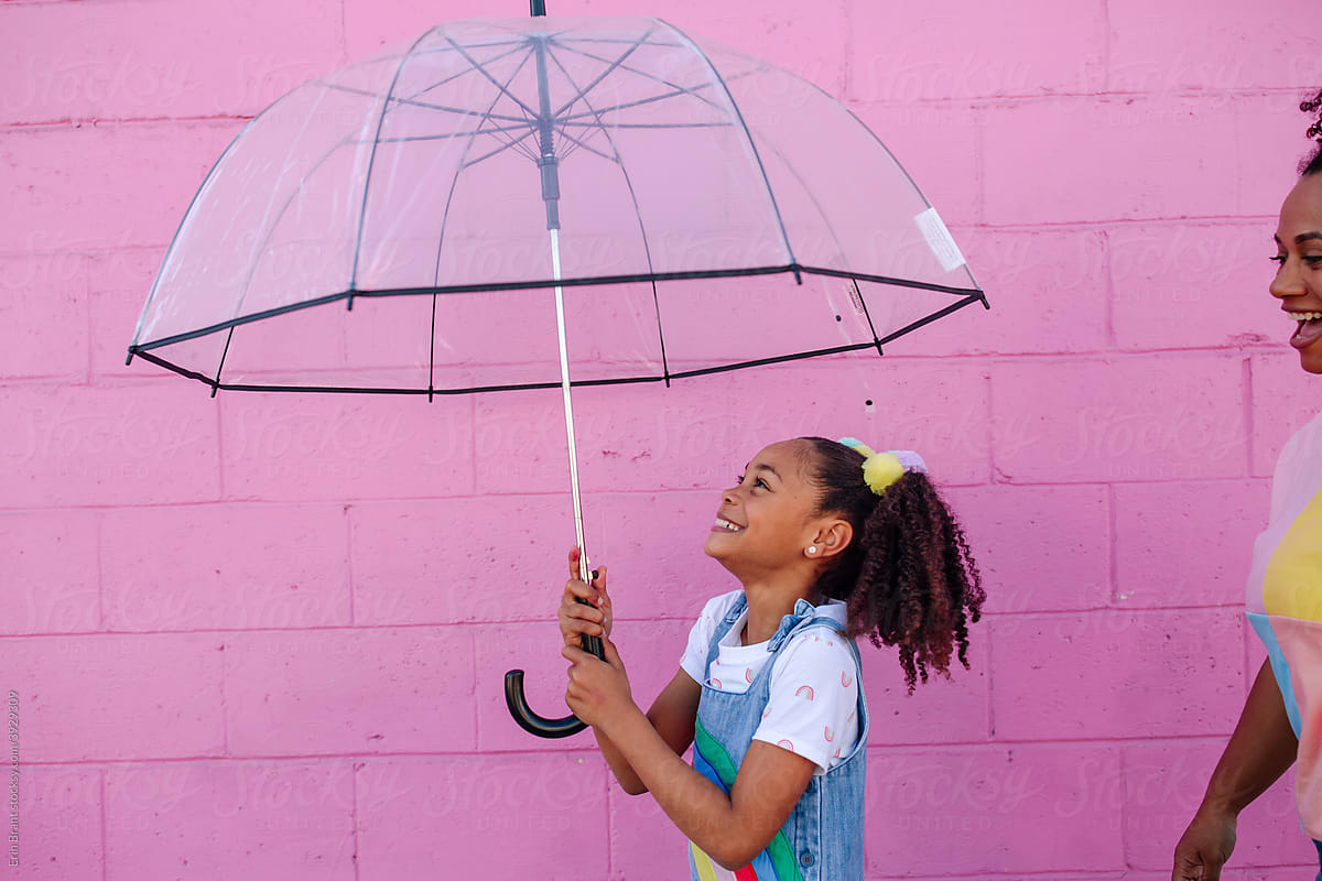Pink wall behind happy girl with umbrella