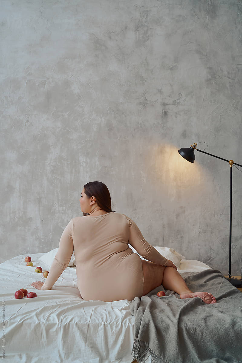 portrait of an Asian woman in a swimsuit sitting on a bed with her back to the camera