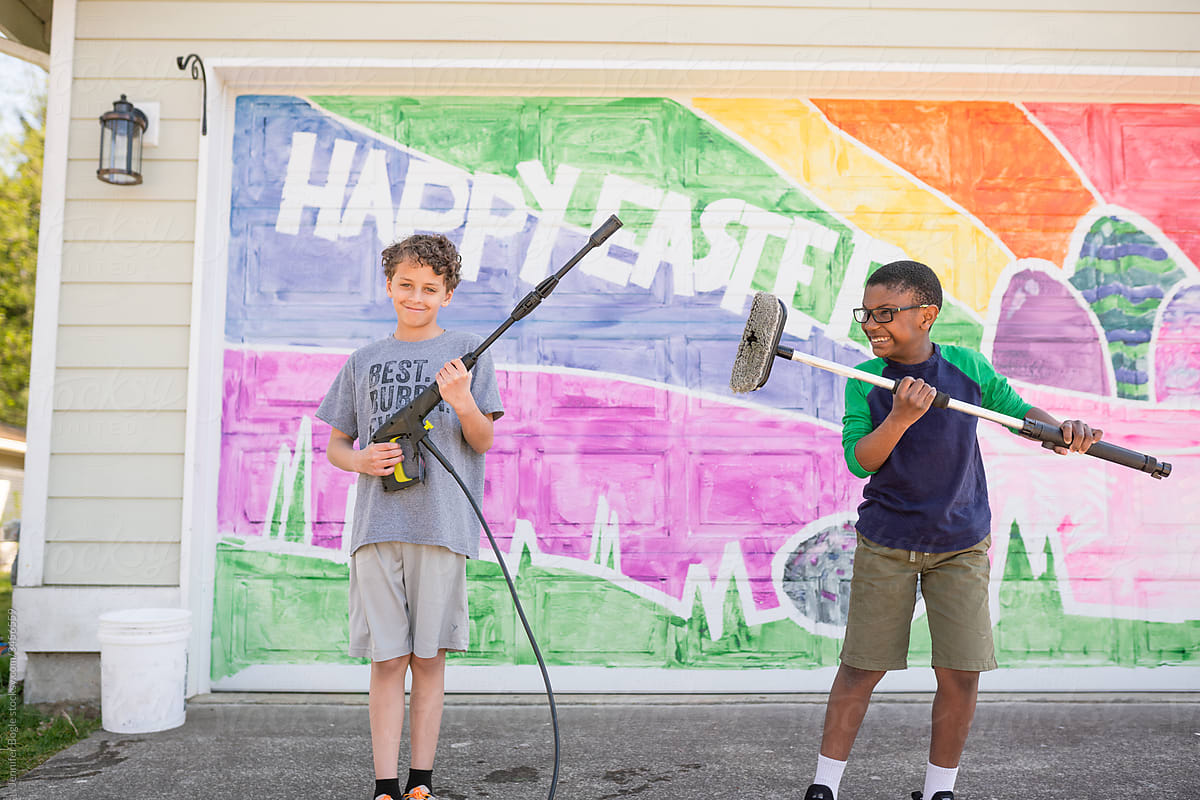 Multiracial brothers hold scrub brush and power washer in front of mural