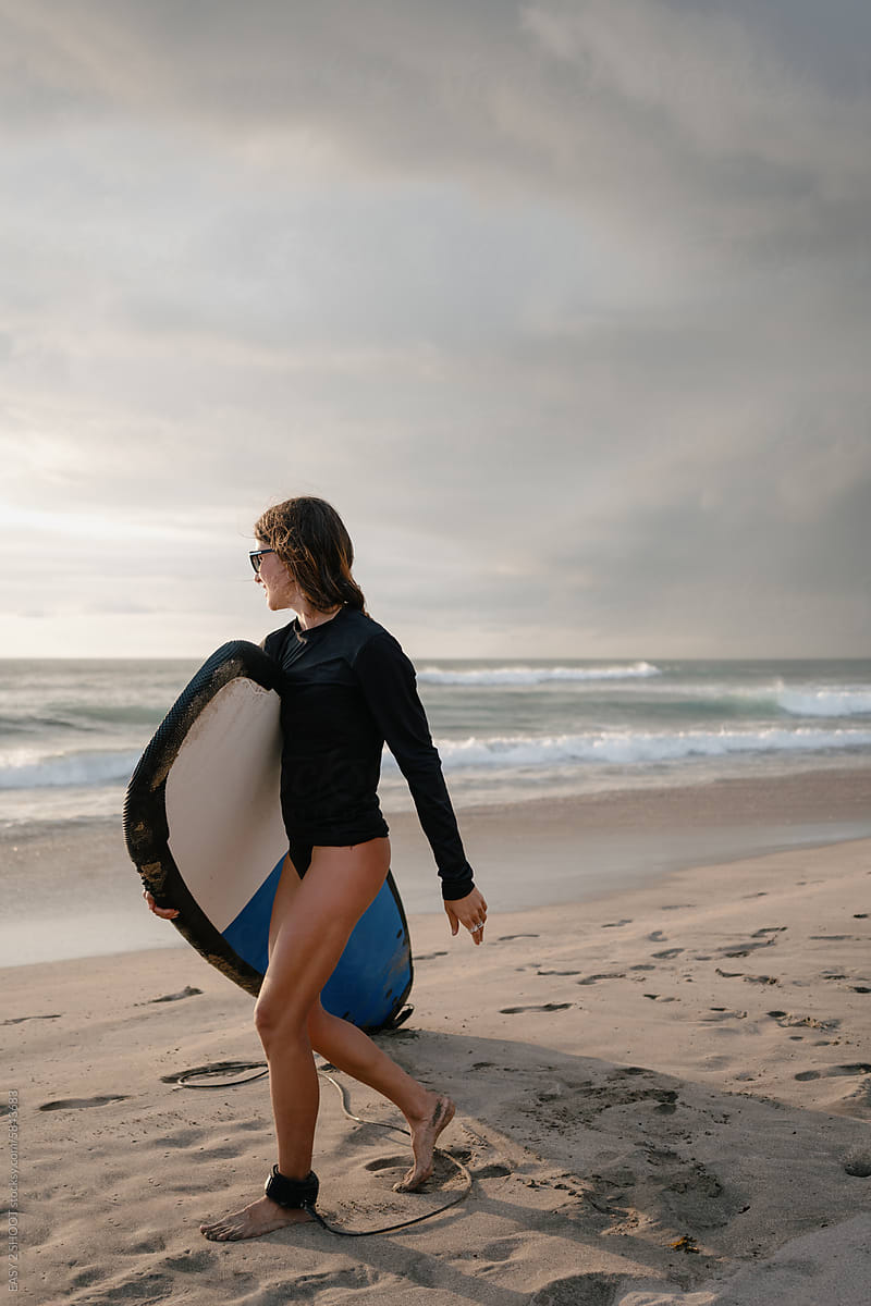 Young Surfer Walking Towards the Waves at a Sandy Beach During Sunset