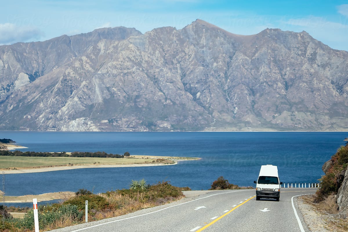 Van drives on lakeside highway with clear view of mountains