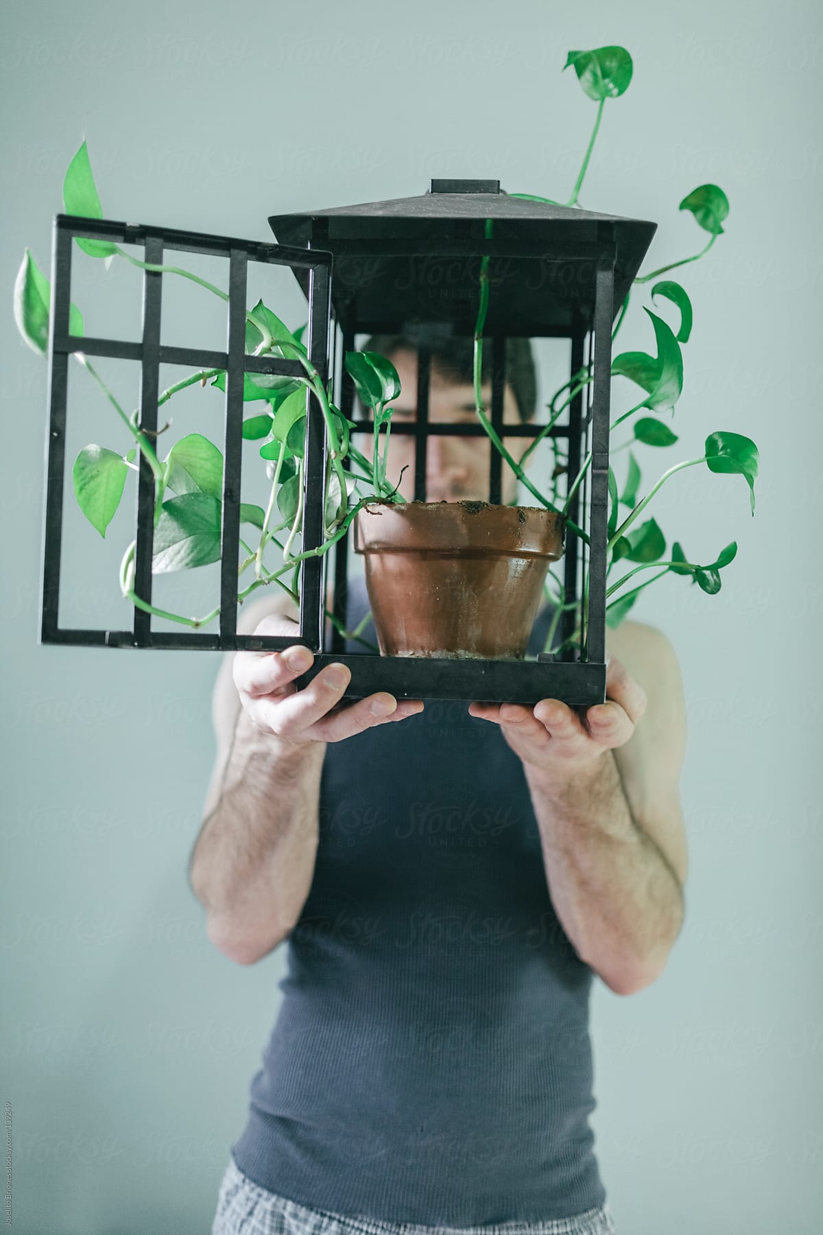 Man Holding Open Lamp Cage with Potted Plant Inside