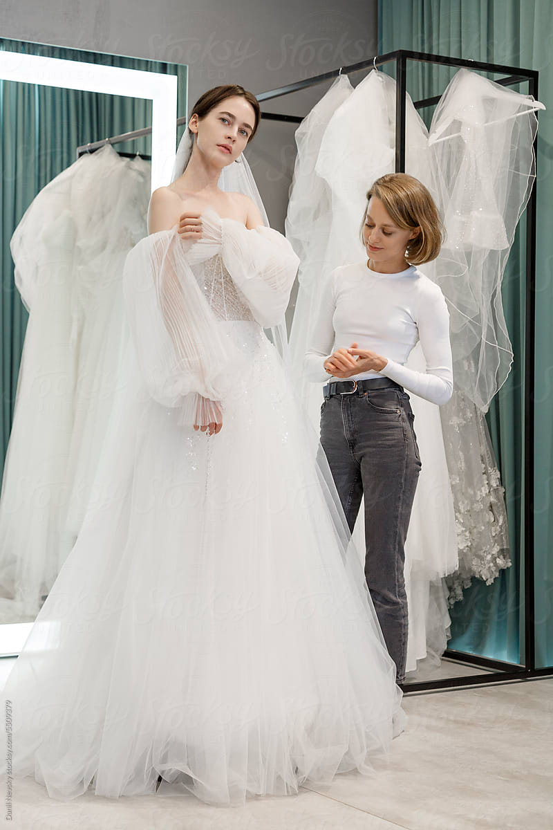 Show owner with bride trying wedding dress in room