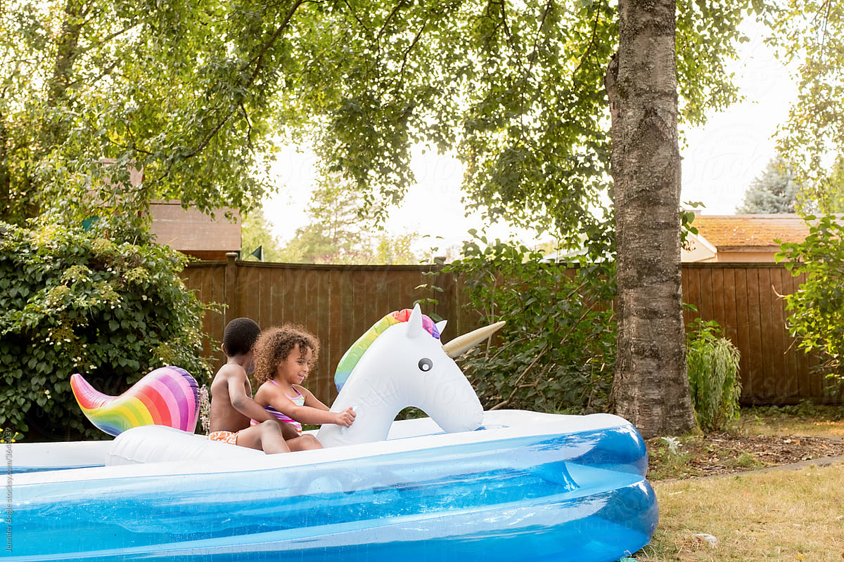 Siblings ride unicorn floatie in small back yard pool