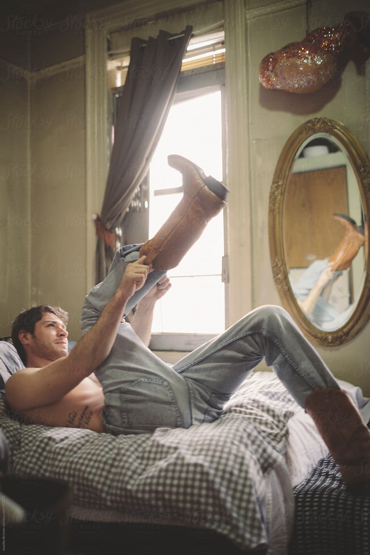 Shirtless Man in Jeans Struggling to Put Boots on in Bed