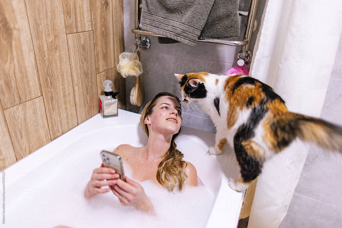 Woman playing with multicolored cat while relaxing in water with foam