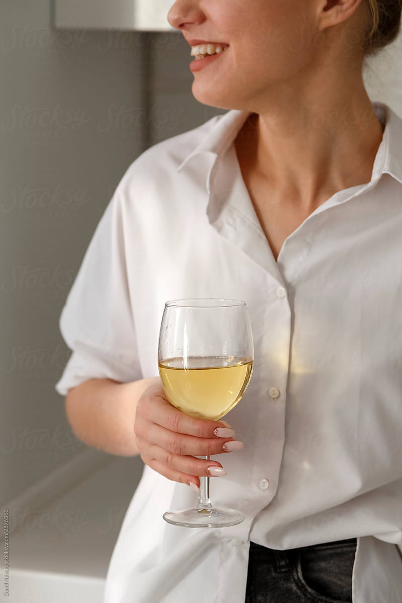 Stylish woman with glass of wine smiling in kitchen