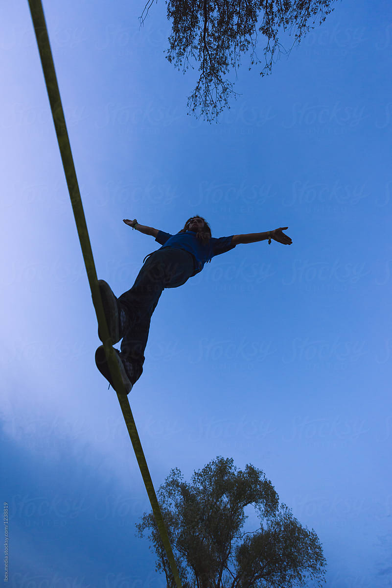 Silhouette of man keeping balance on slackline outdoor during tw