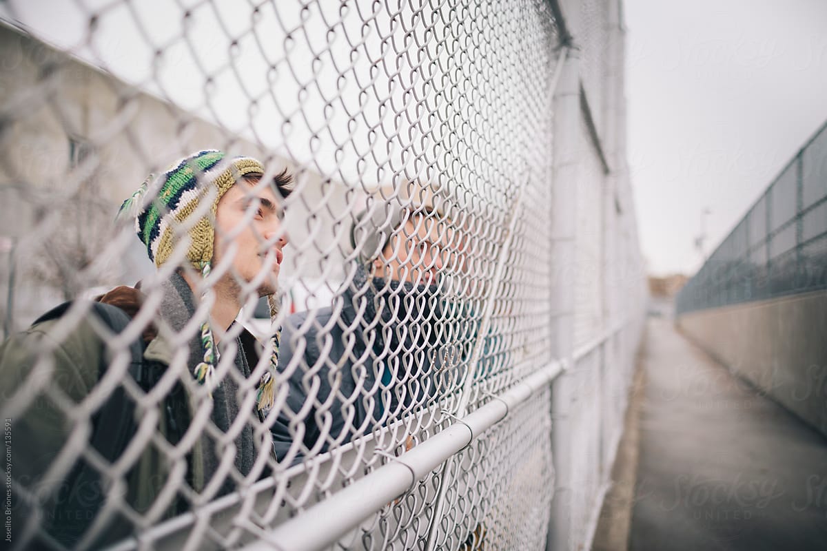 Group of Young Men Friends Watching Through Chainlink Fence