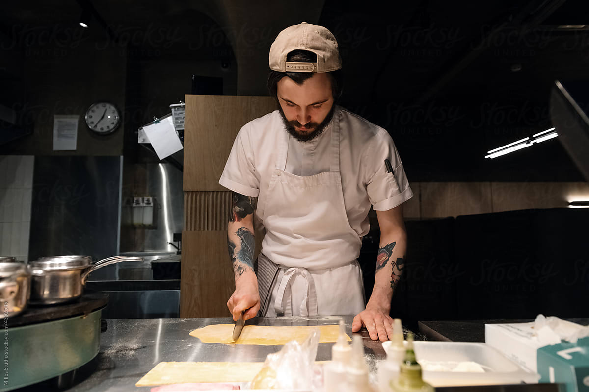 Tattooed cook cutting pasta dough