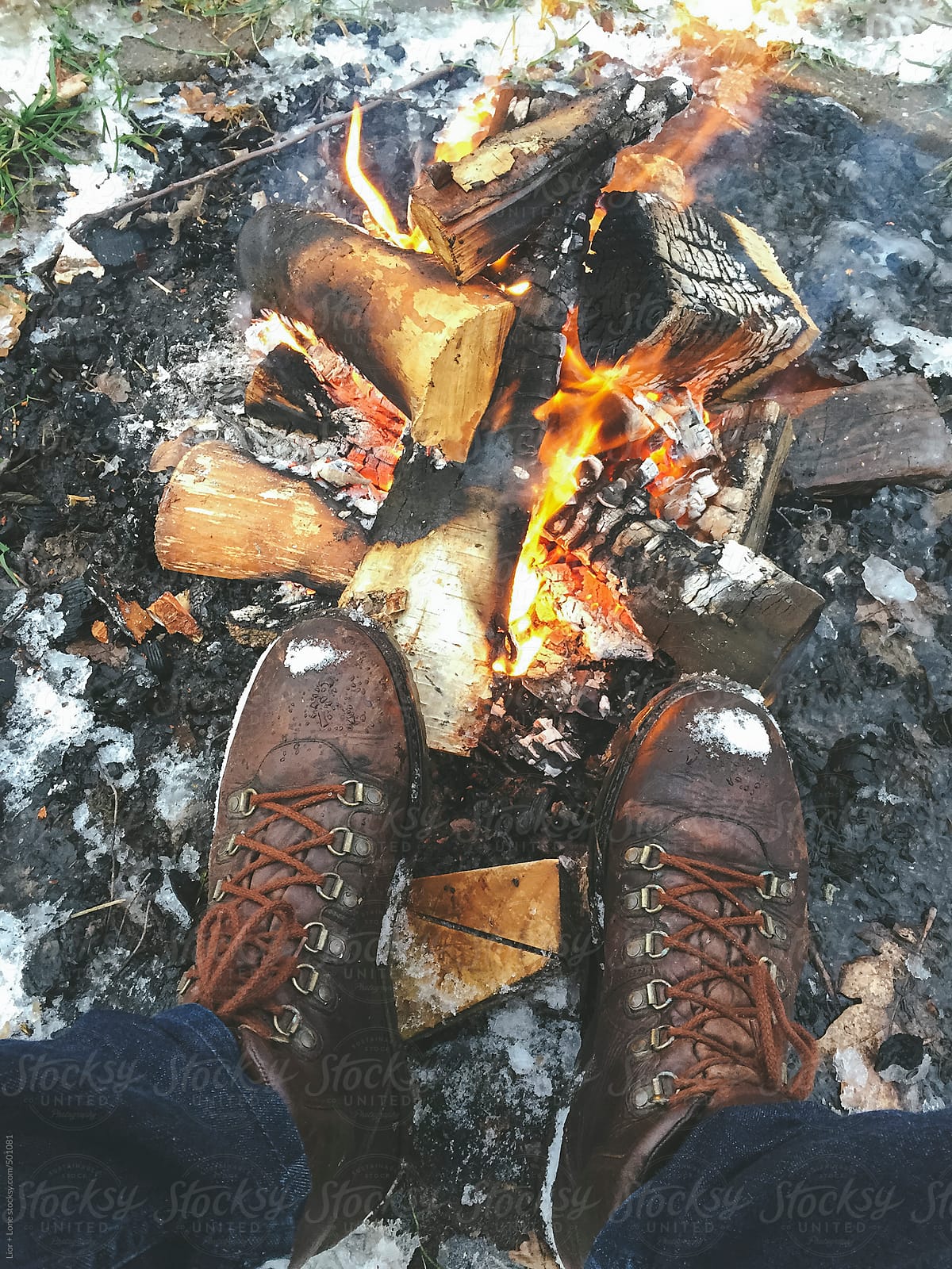 Man’s legs in boots next to fire in the snow