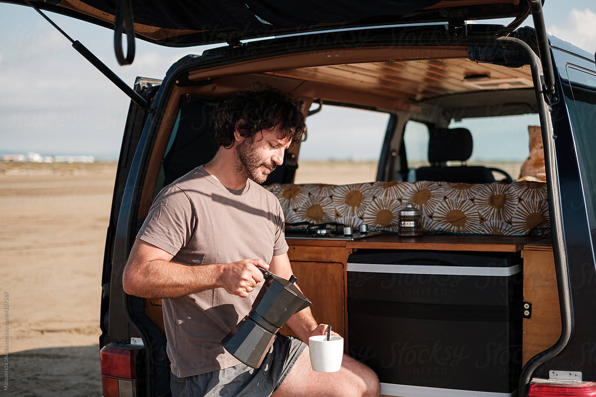Man drinking coffee in camper van on beach