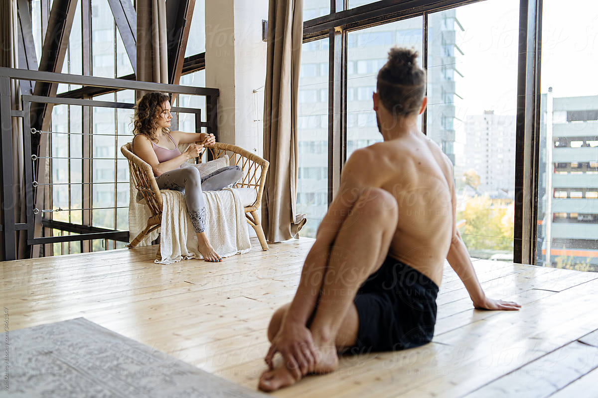 Man doing yoga near woman using smartphone