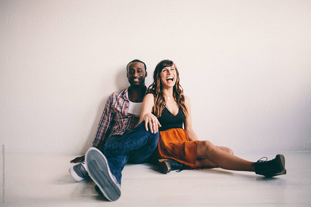 Cute Young Interracial Couple Laughing Sitting On Apartment Floor Stocksy United