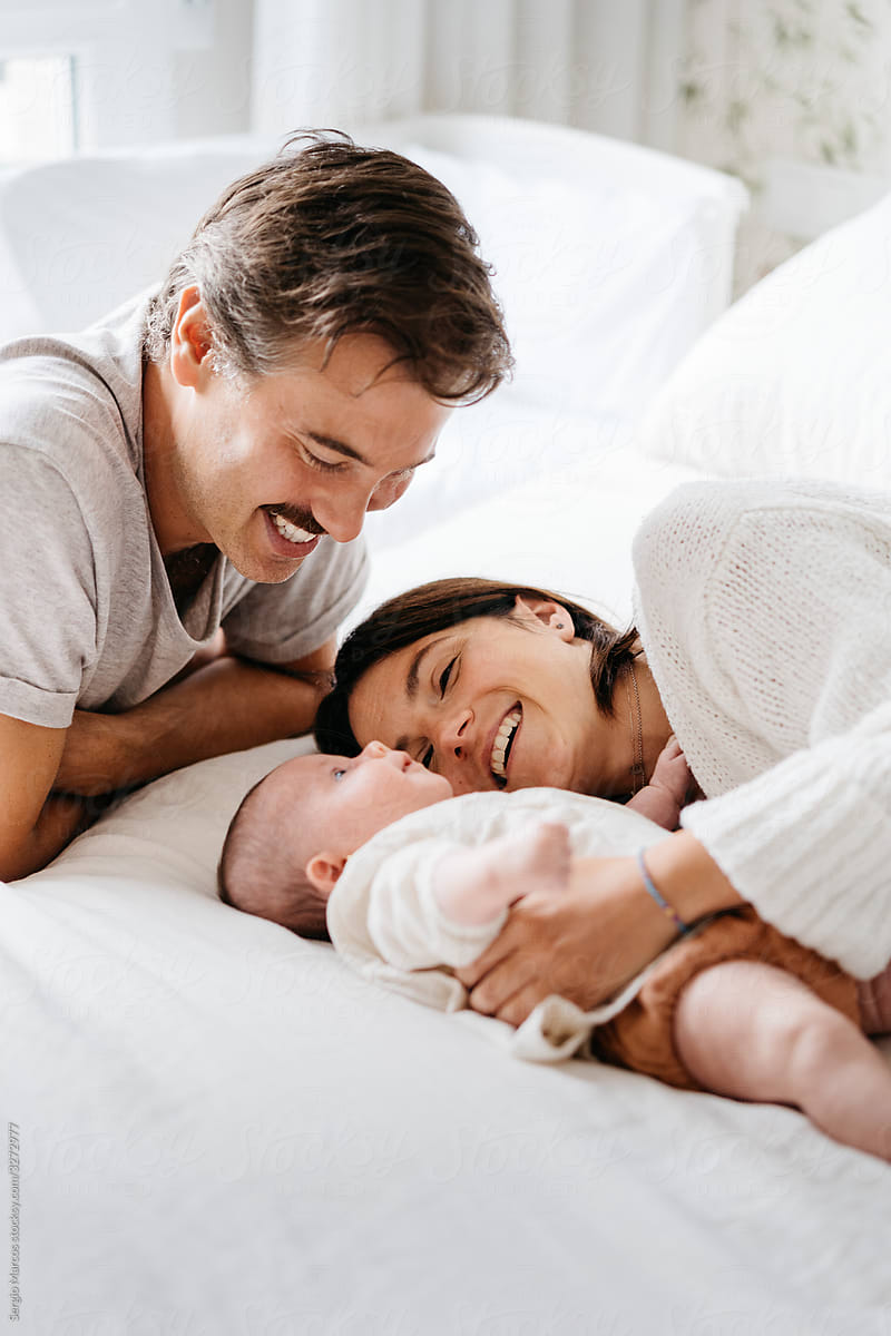 parents lying on bed with baby in cozy sunny bedroom