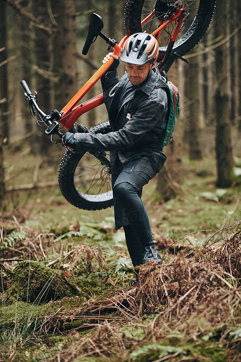 Mountain biker walking through a forest carrying his bike