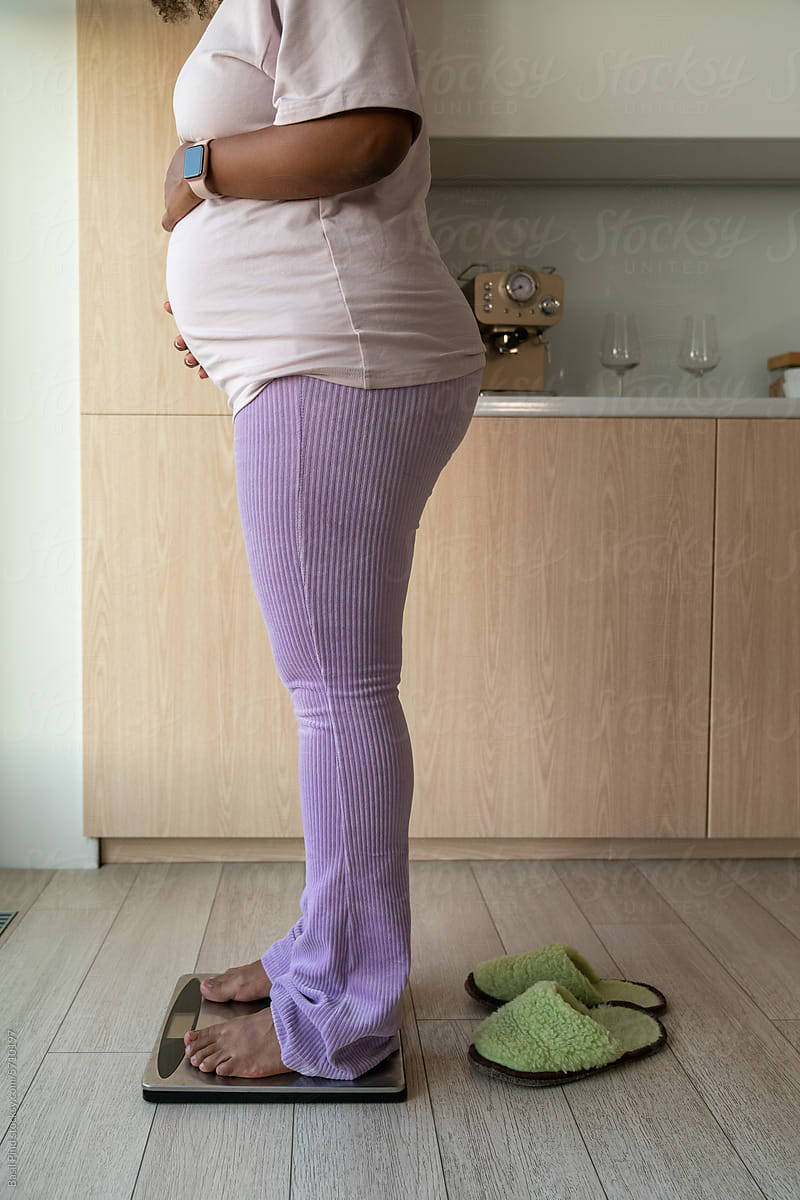 Pregnant woman standing on a scale in the kitchen