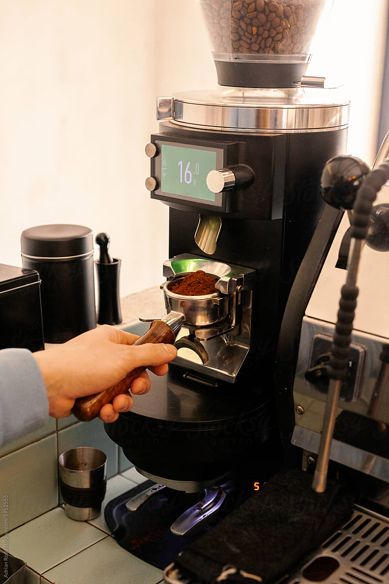 Close-up of a barista\'s hand using an electric coffee grinder