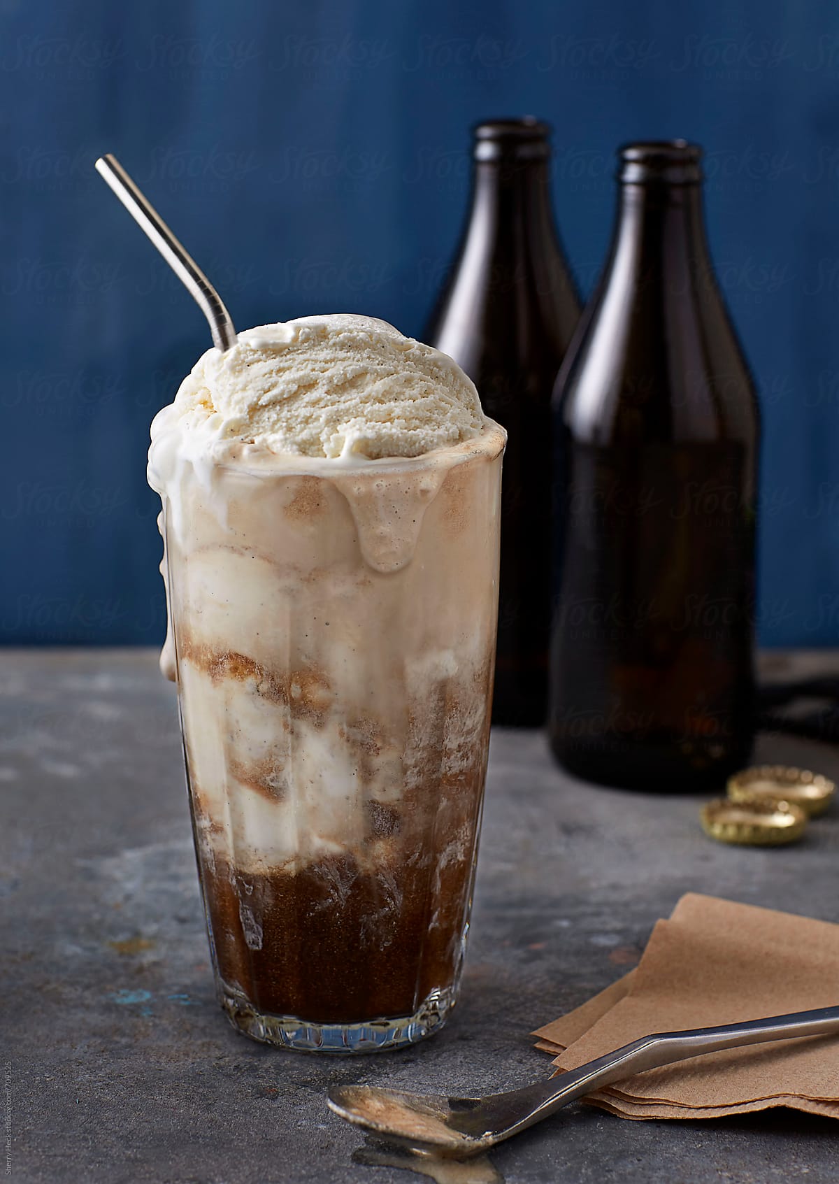 Vanilla ice cream float with drip with brown bottles, metal surface and blue background