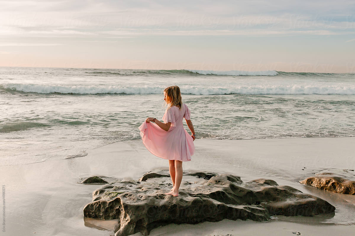 Tween girl in pink dress standing on rock on a west coast beach