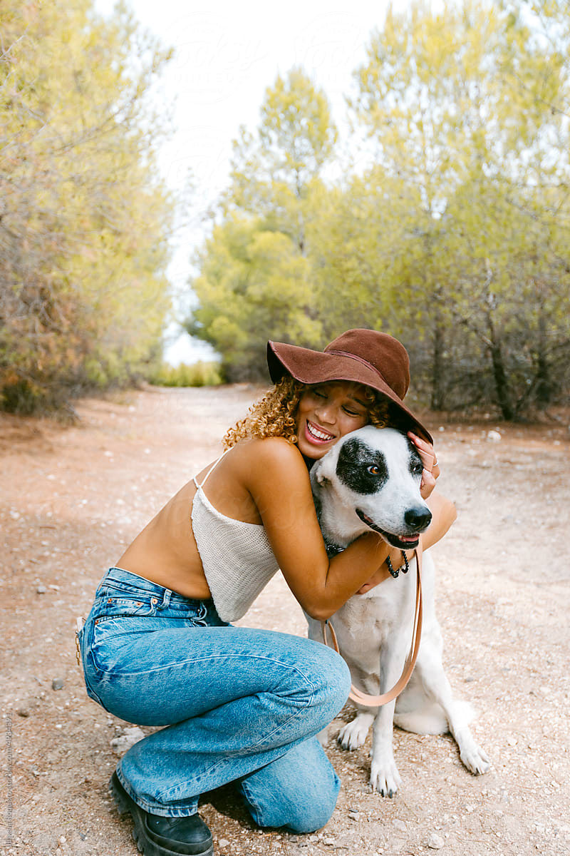 Girl with hat hugging her dog outdoor in sunlight smiling