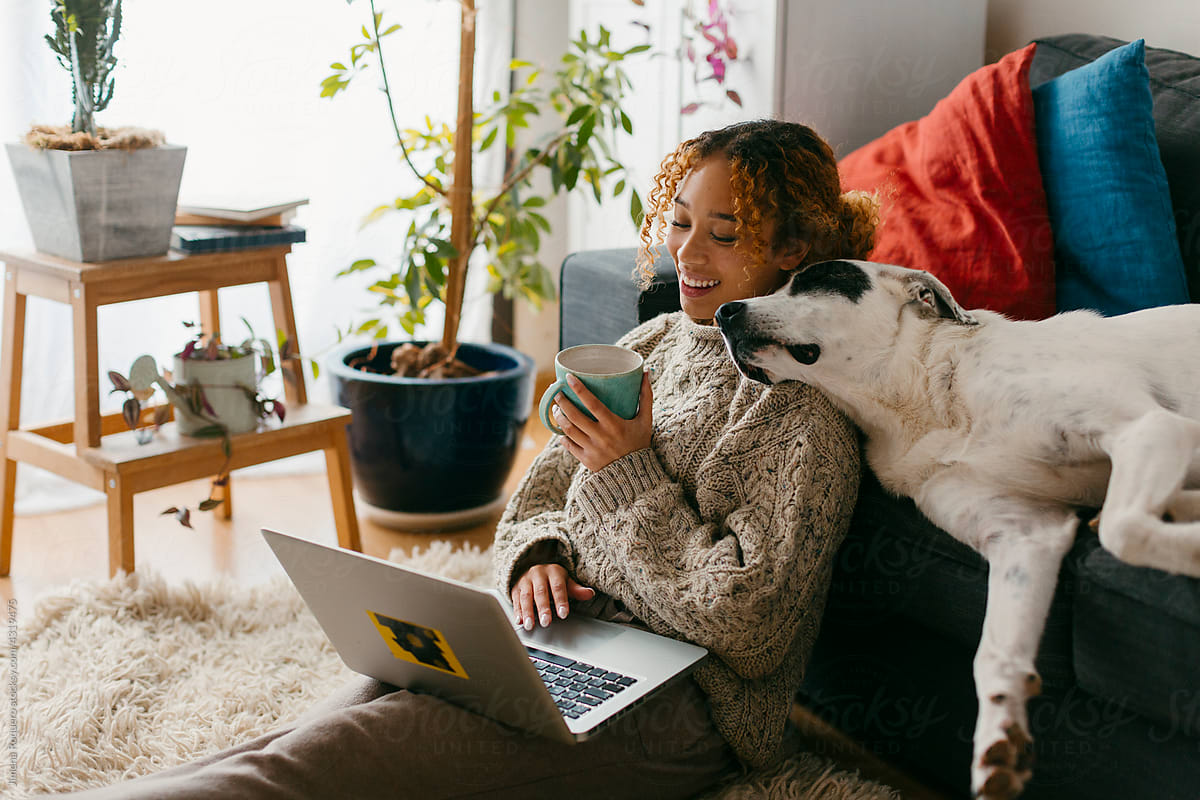Girl smiling using laptop and drinking coffee with dog