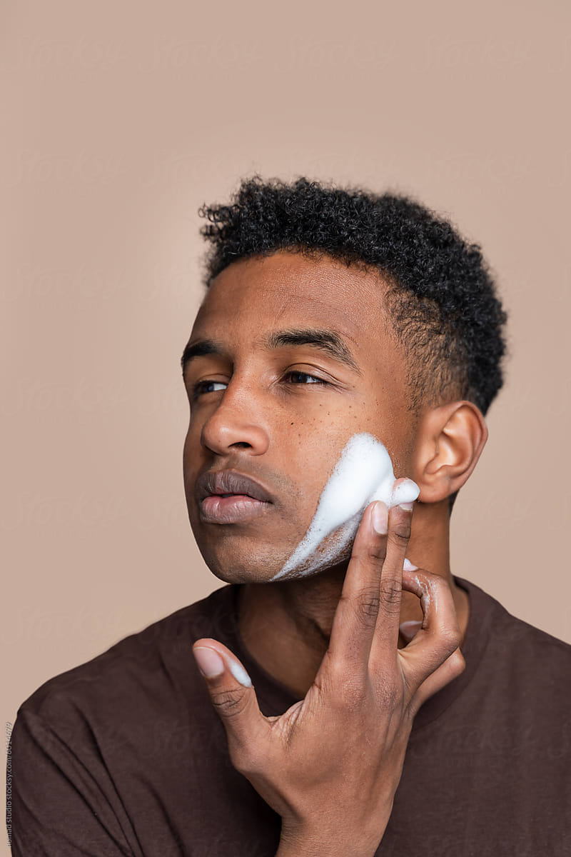 Close-up of a young man gently applying moisturizer to his face