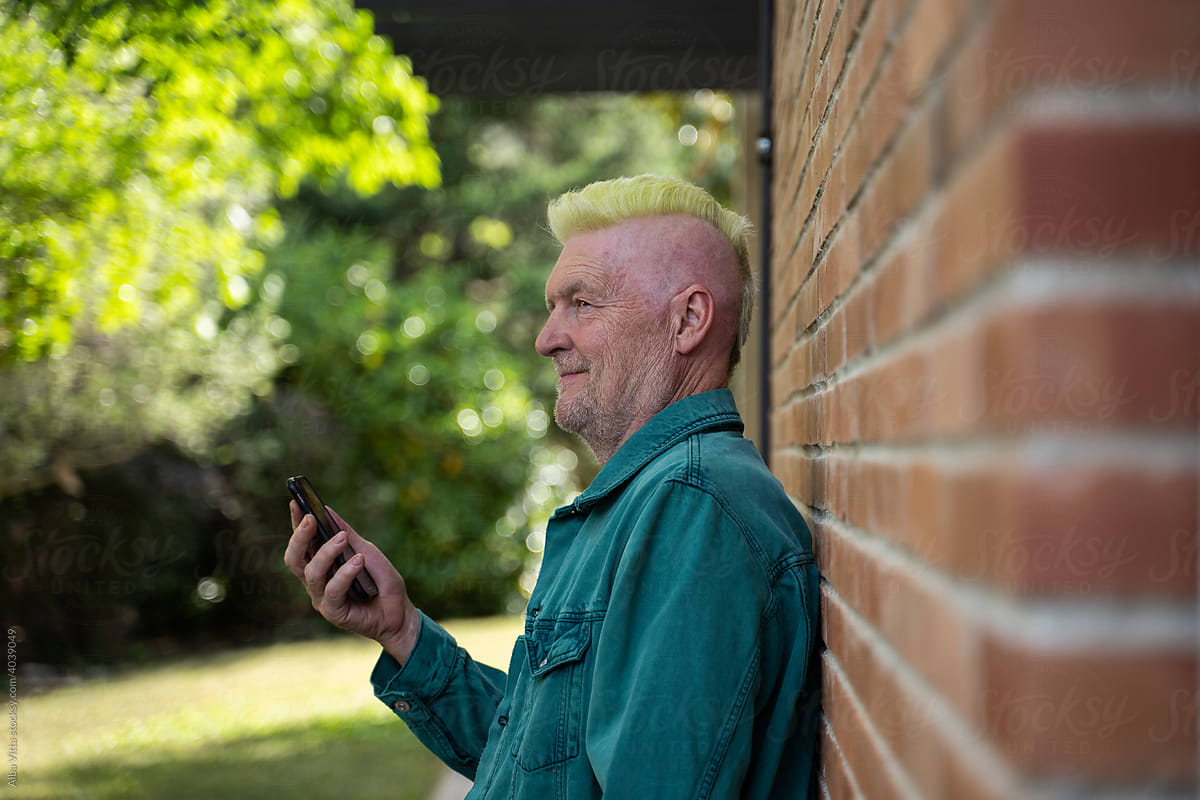 Senior man leaning against wall and holding phone