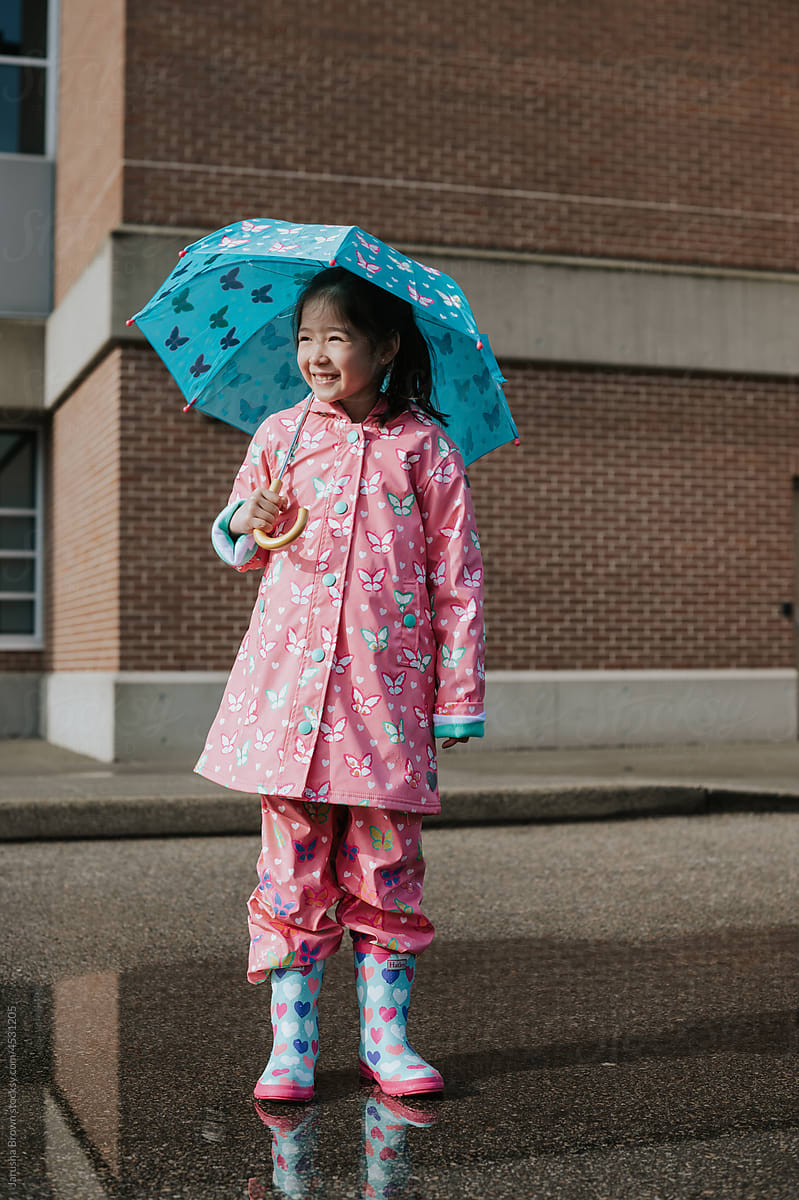 Young girl stands in a puddle with rain boots and an umbrella.