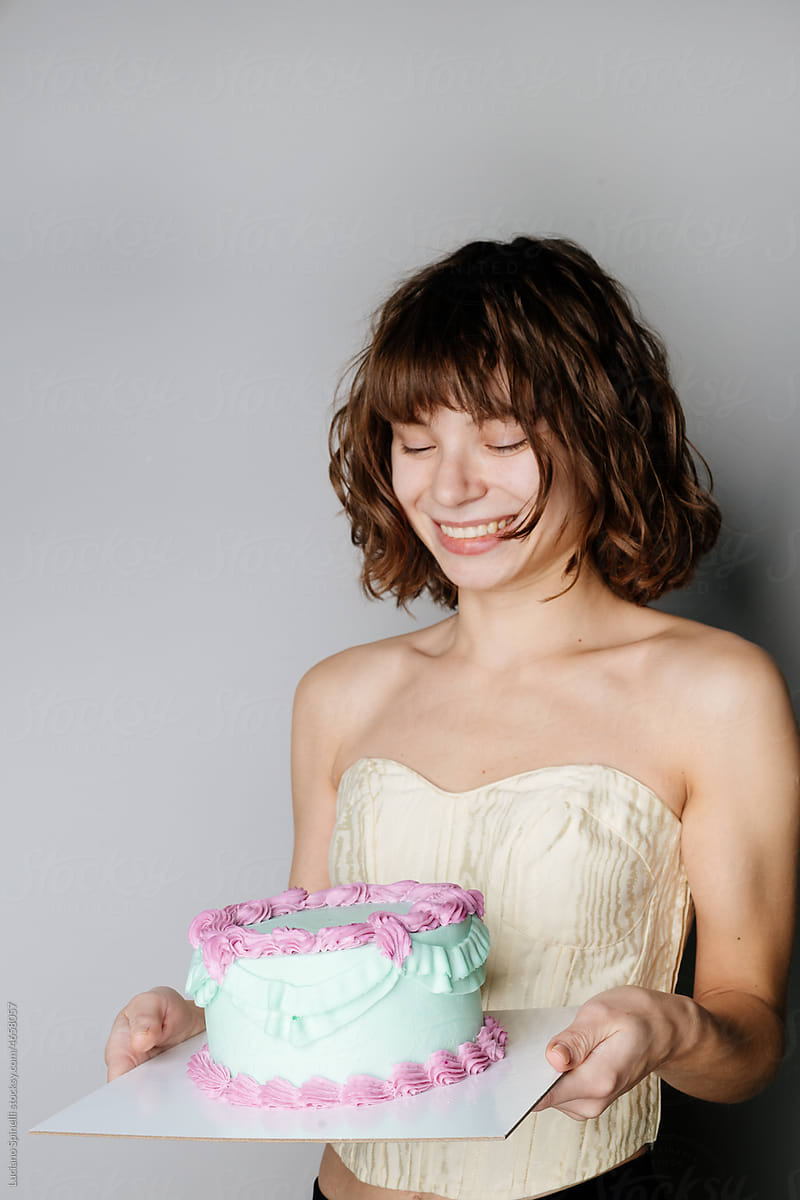 Happy curly girl in beige corset is holding a colourful birthday cake