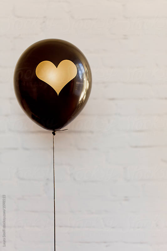 Black latex balloon decorated with gold heart floats in front of white brick wall