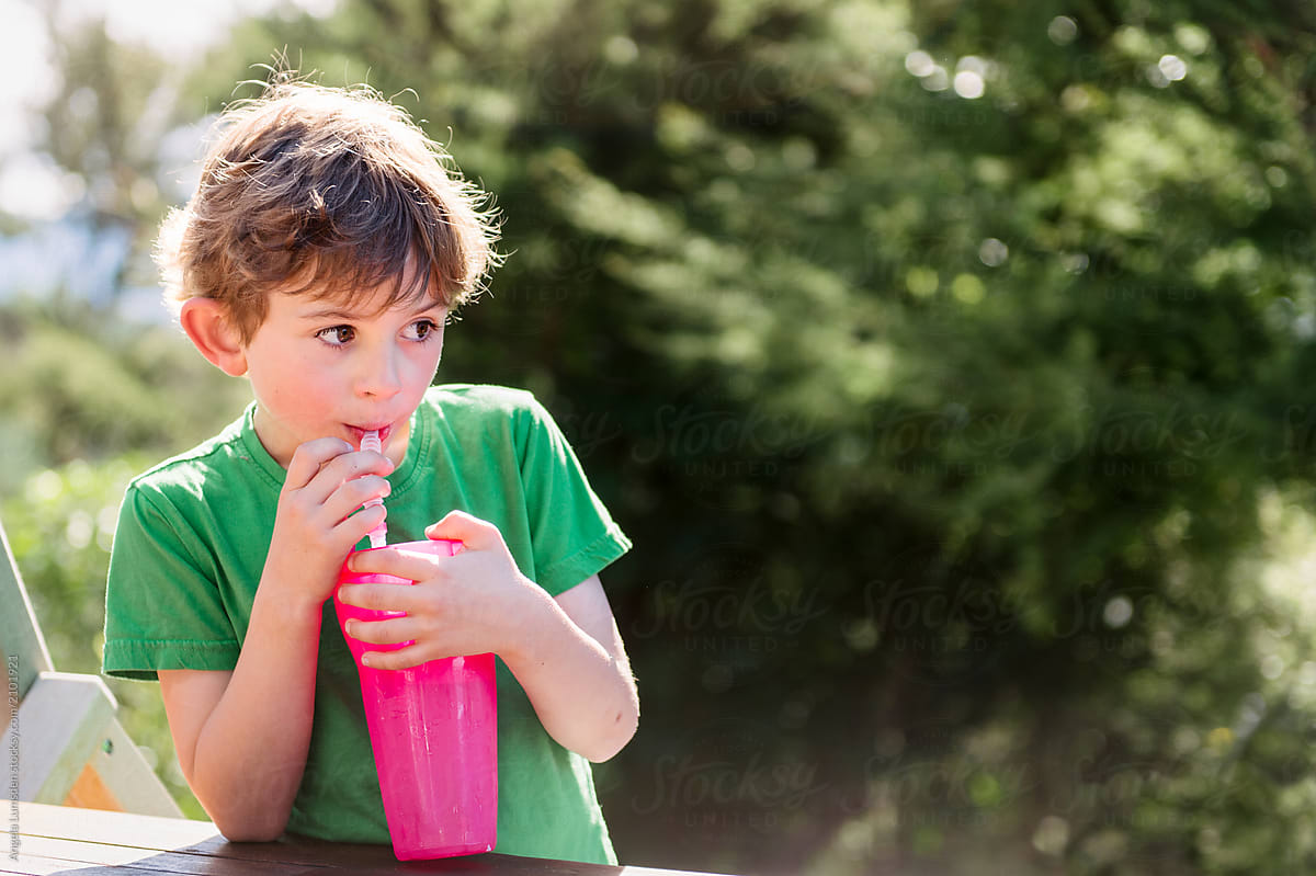 Boy drinking from a pink drink bottle outdoors on a sunny day