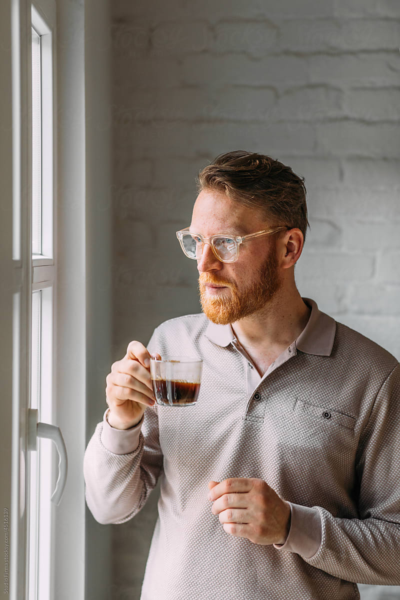Man Looking Through Window and Drinking Coffee