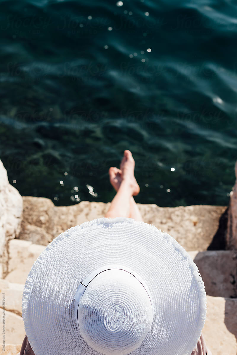 Woman behind a white hat sunbathe her feet