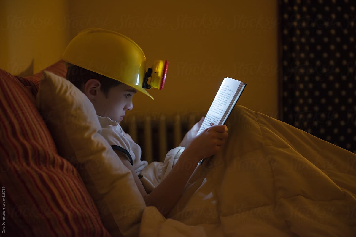 Child wearing a headlamp reads in bed