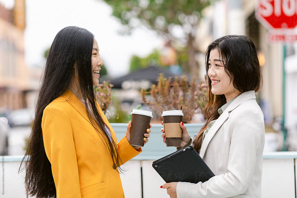 Cheerful Chinese colleagues enjoying coffee to go on street