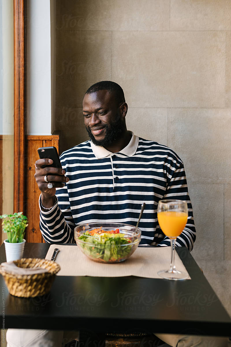 Happy black man using his smart phone inside a bar