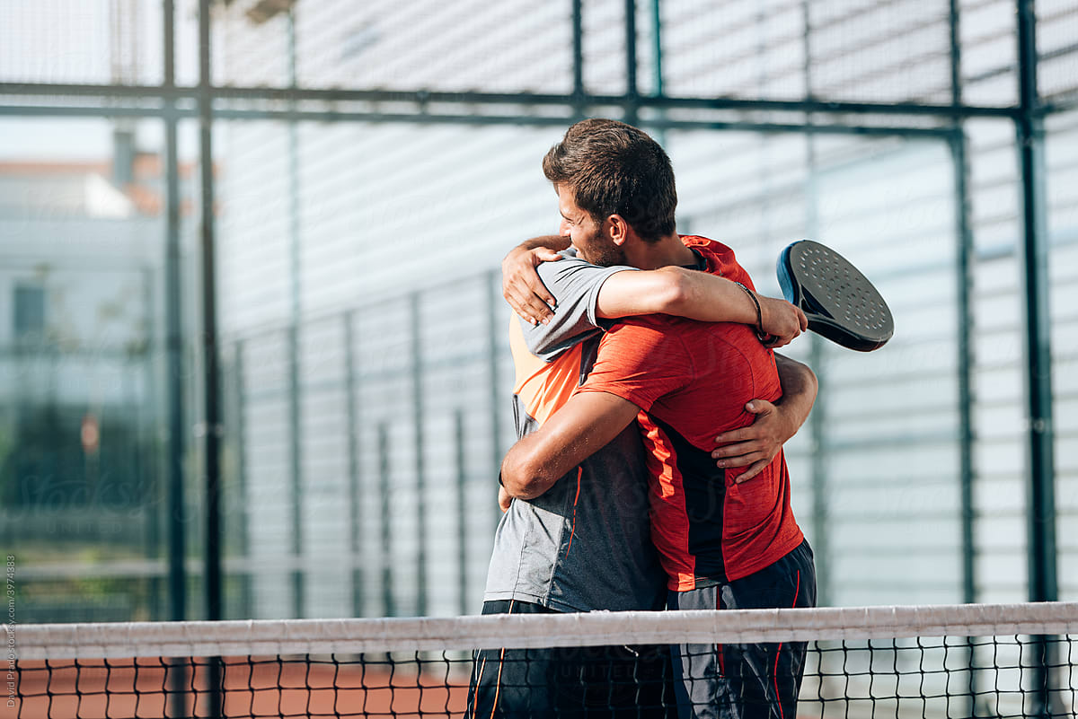 Happy men embracing near net in court after win a padel tennis match