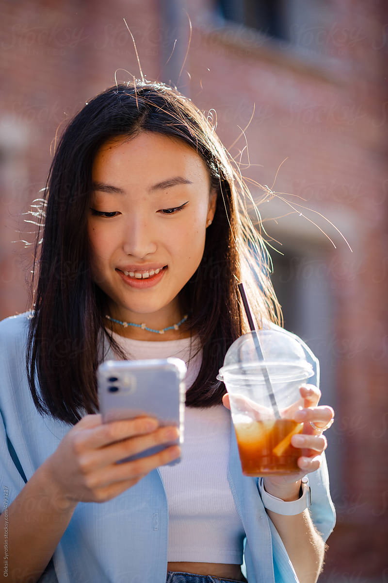 Girl with takeout drink checking cellphone