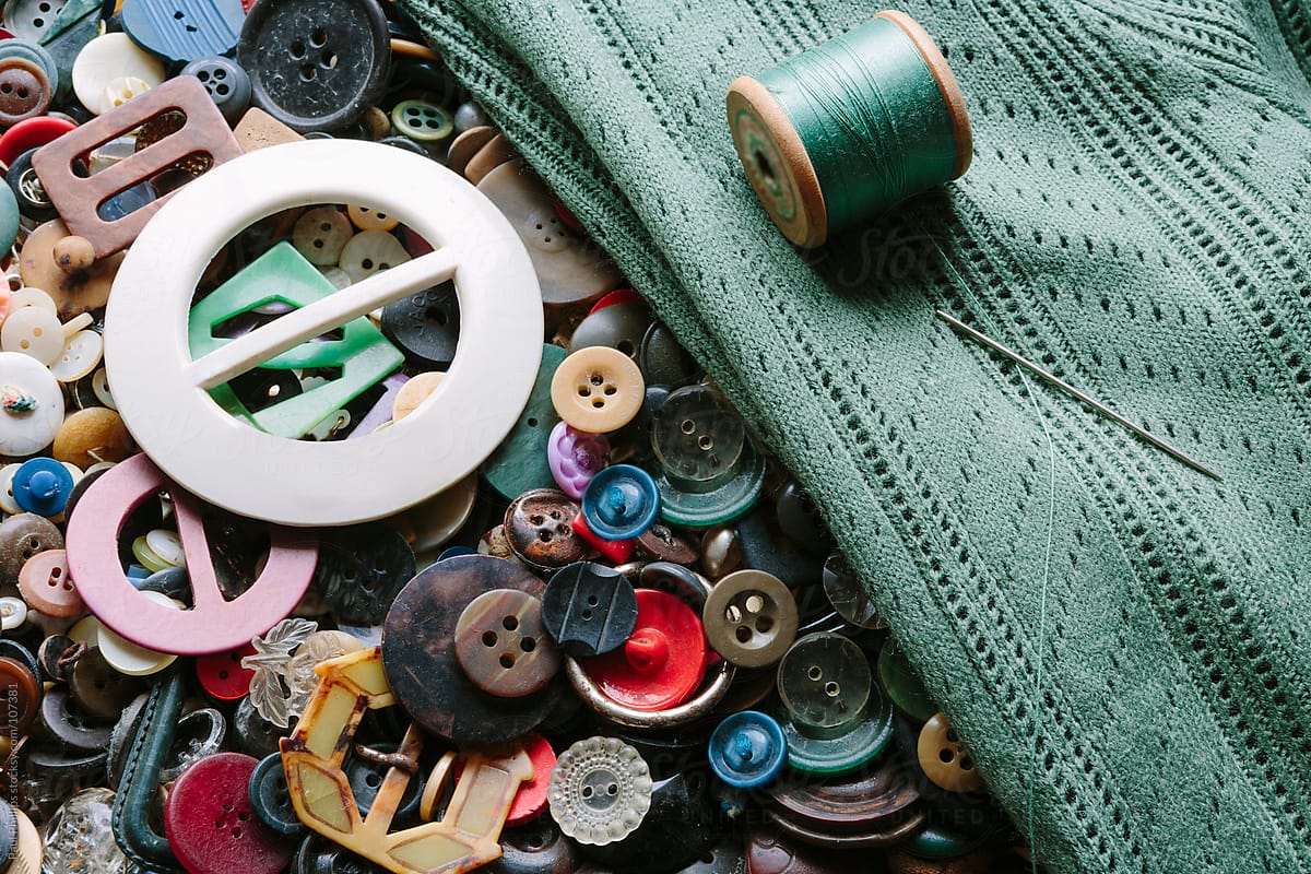 Collection of antique and vintage buttons and buckles, green cardigan being repaired