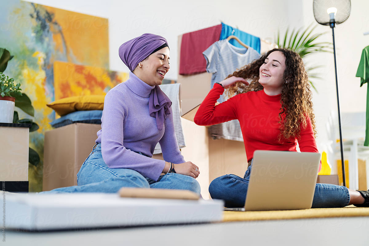 Cheerful diverse women using laptop in new apartment