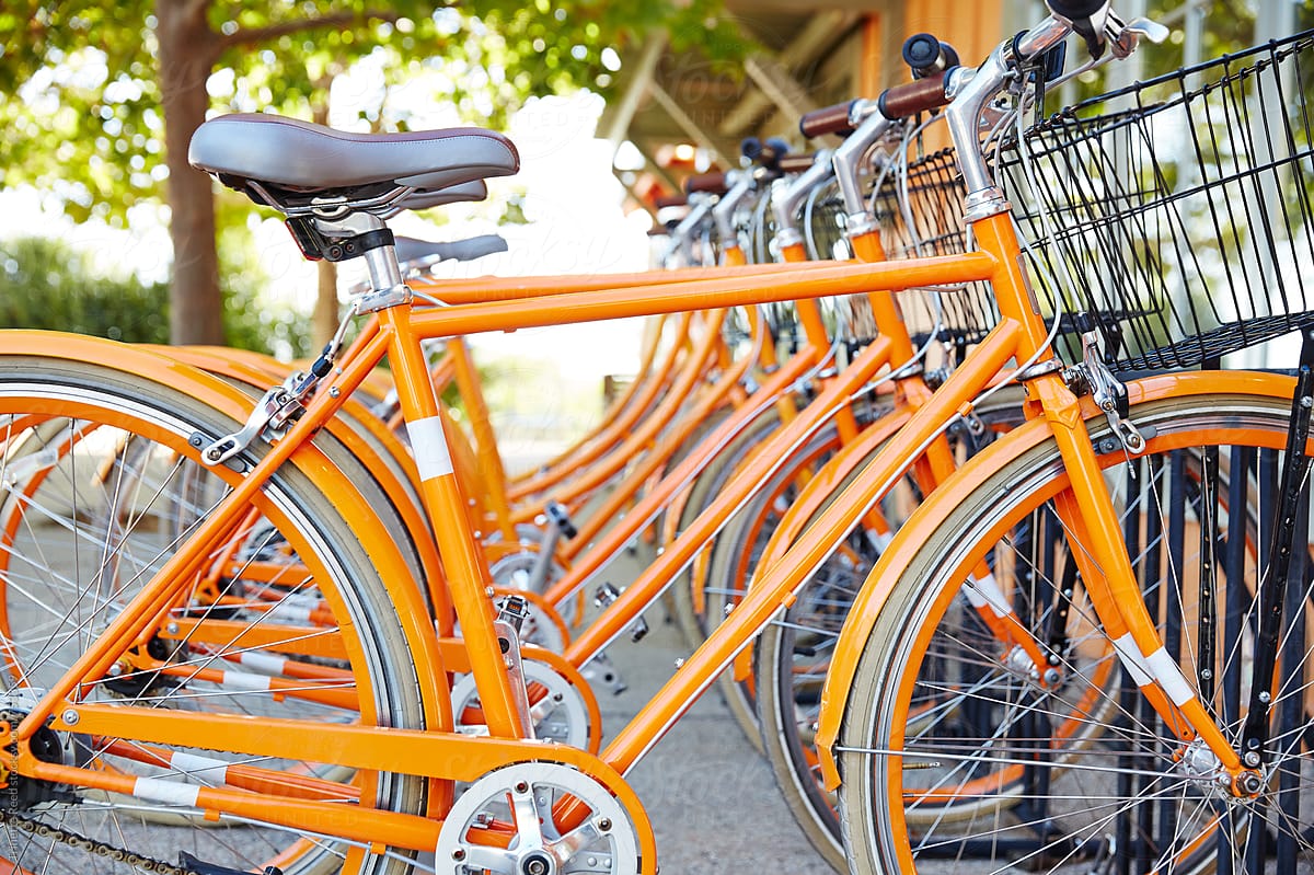 Row of orange cruiser bikes with baskets