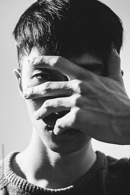 Closeup portrait of an asian man covering his face. Black and white photo.