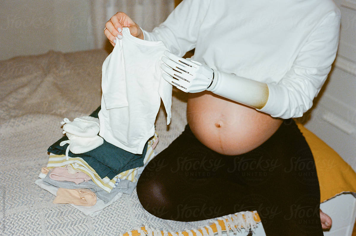 Maternity leave. Close up pregnant woman hold at newborn clothes.