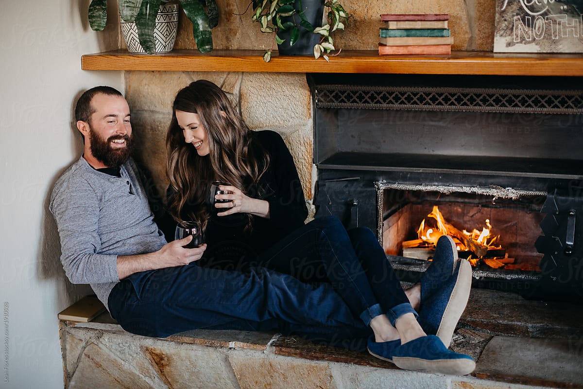 Happy Couple Sitting by Fireplace Drinking Wine