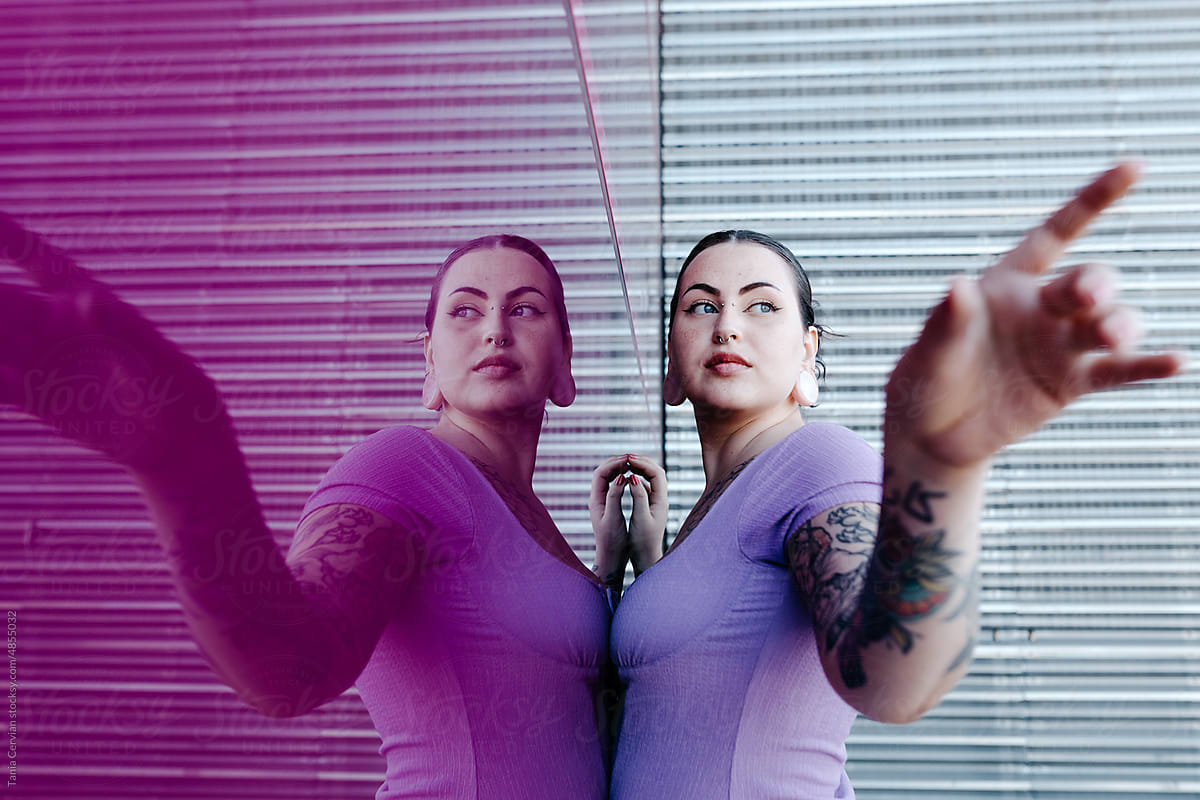 Self assured tattooed woman standing near glass wall