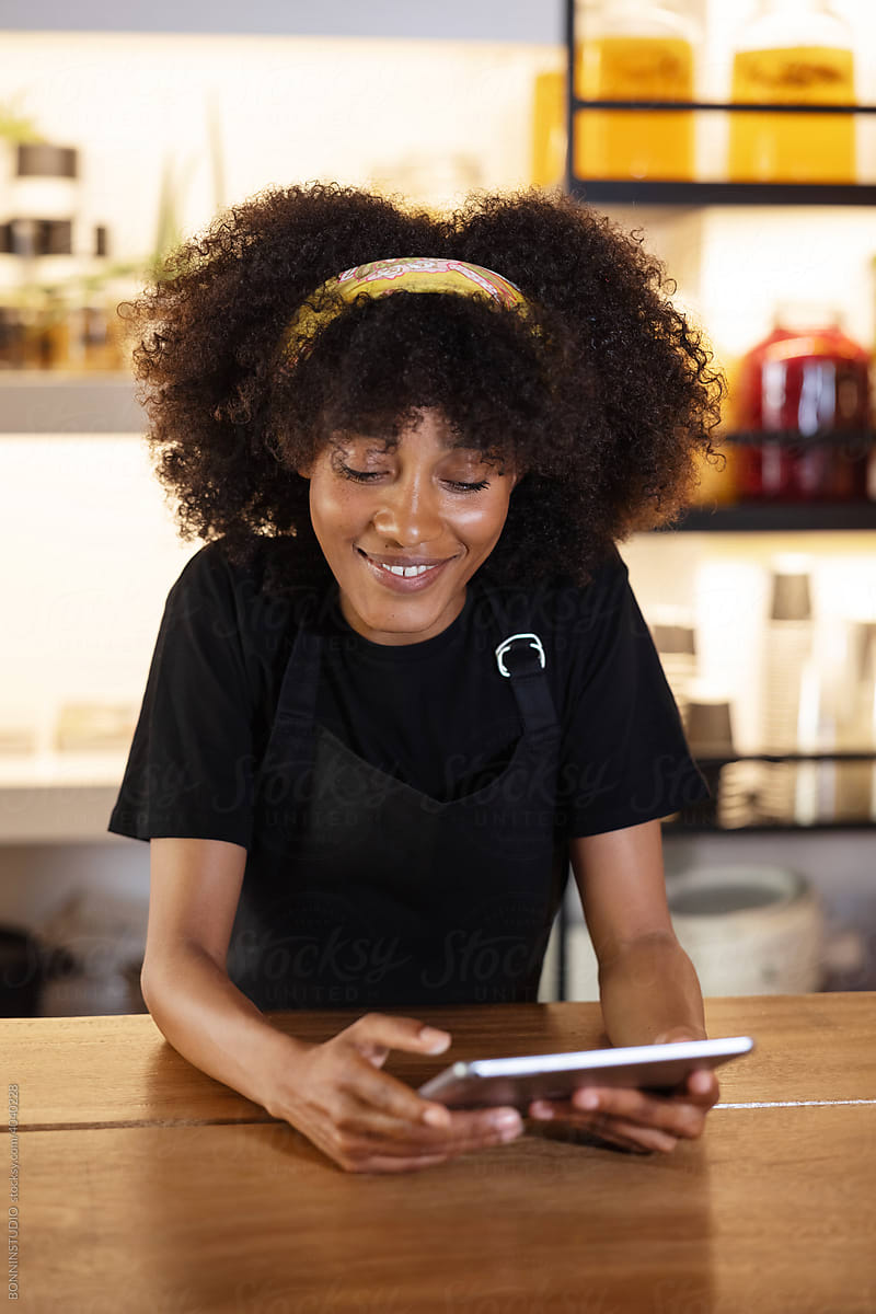 Smiling black waitress using tablet and working in cafe