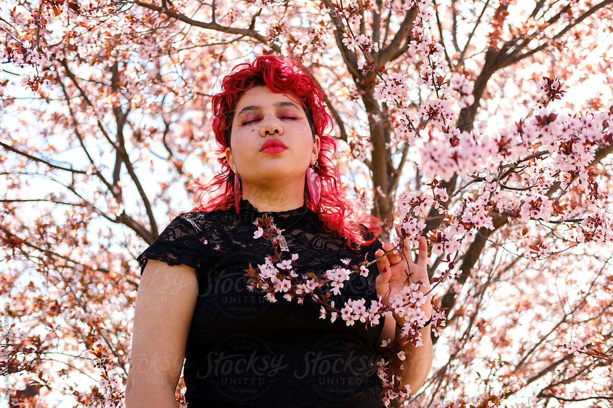 Queer person posing behind almond tree in blossom with eyes closed