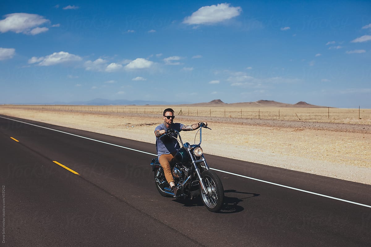 Man heads down open desert road on motorcycle