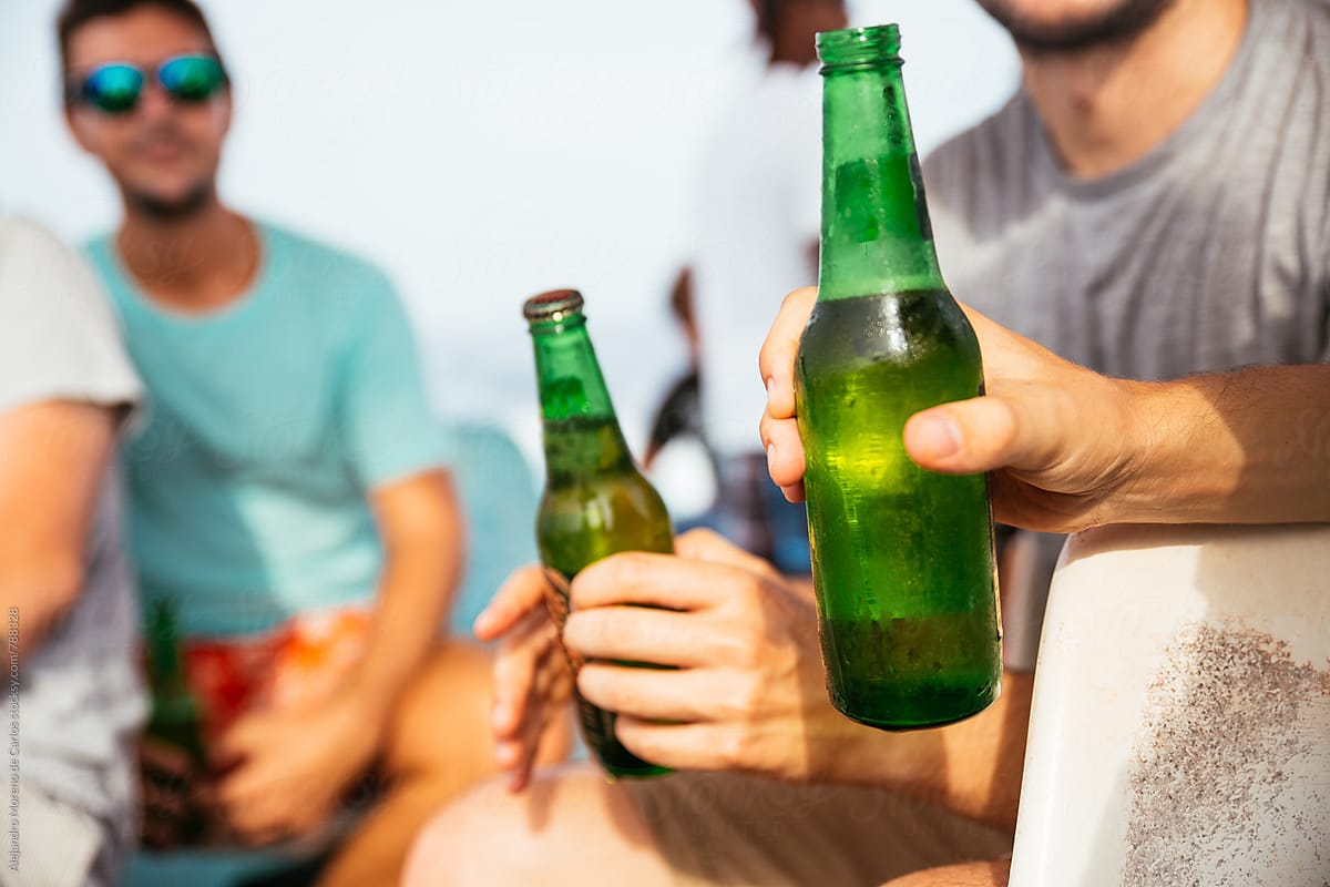 Front view of male hands holding green beer bottles outdoors on a sunny day